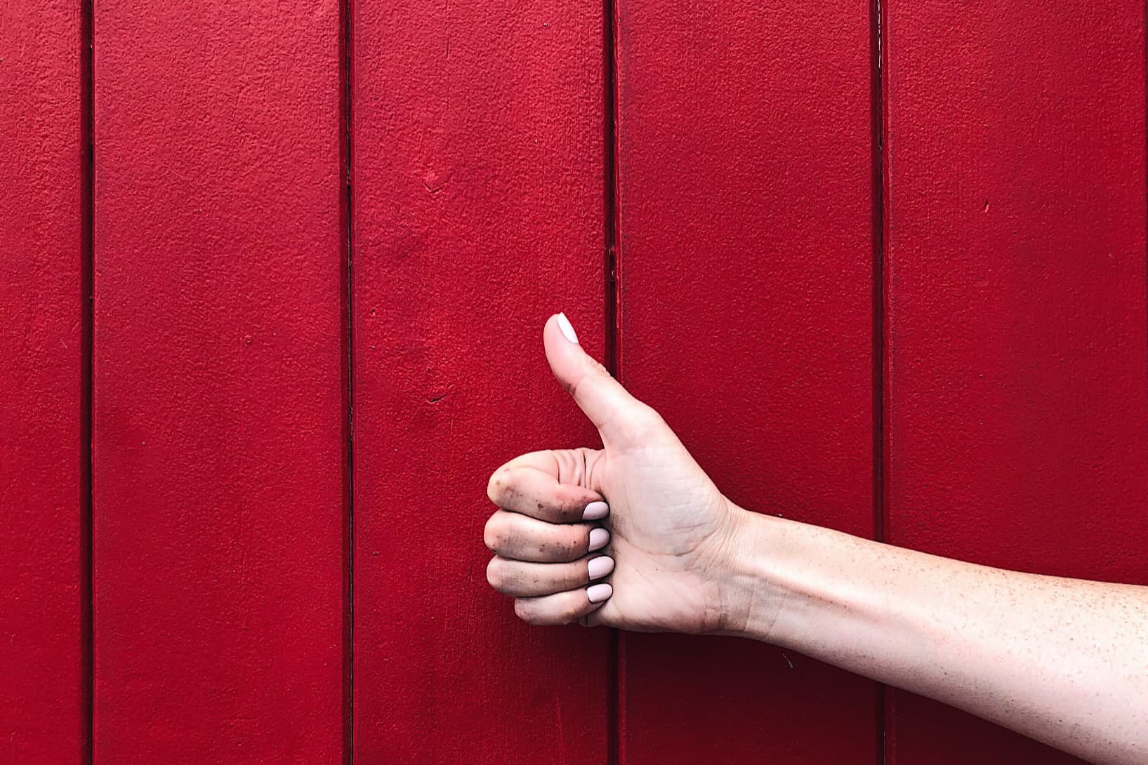 A hand doing a thumbs up in front of a red wall.